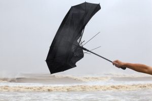 Close-up of hand struggling with broken umbrella in wind near the sea.